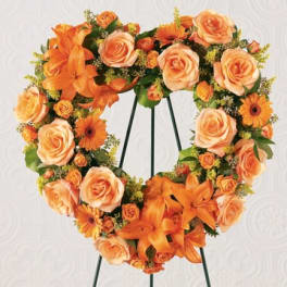 Heart-shaped floral wreath with orange roses and lilies on a stand