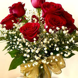 Red roses and baby's breath in a glass vase with a gold ribbon