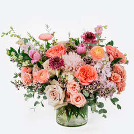 Mixed pink and peach flowers arranged in a clear glass vase