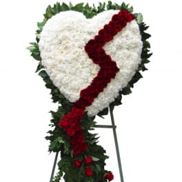 Heart-shaped white floral spray with a red rose ribbon on a stand