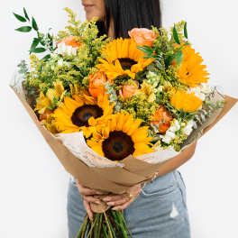 Bouquet of sunflowers, peach roses, and white flowers wrapped in brown paper