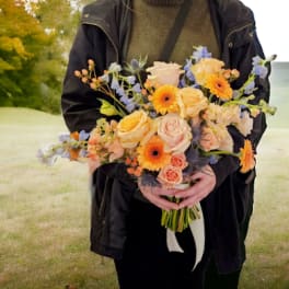 Person holding a bouquet of peach, pink, and orange flowers