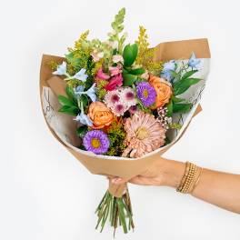 Handheld bouquet of mixed pastel flowers wrapped in brown paper