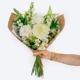 Handheld bouquet of white roses and pale blooms wrapped in brown paper