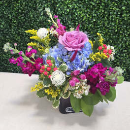 Mixed bouquet with a pink rose, blue hydrangea, and bright magenta flowers in a black container