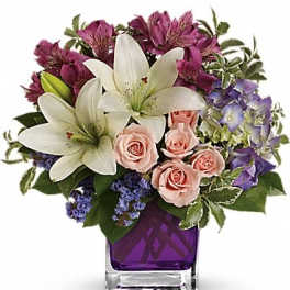 Bouquet of white lilies, pink roses, and purple flowers in a purple glass vase