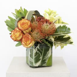 Orange roses and red pincushion blooms in a glass vase