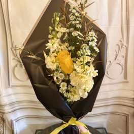 Bouquet of yellow and white flowers wrapped in black paper with a yellow ribbon
