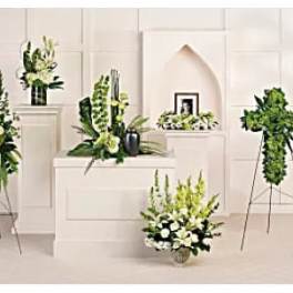 Multiple white and green floral funeral arrangements on stands and pedestals