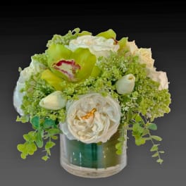 White and green floral arrangement in a clear glass vase with orchids and roses