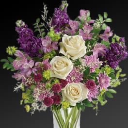 Bouquet of white roses and purple flowers in a clear glass vase