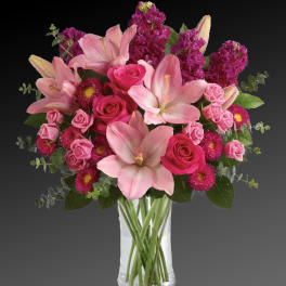 Pink lilies and roses arranged in a clear glass vase