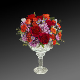 Mixed bouquet of red and orange roses in a clear glass pedestal vase