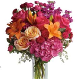 Mixed bouquet of pink, orange, and purple flowers in a clear glass vase