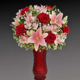 Bouquet of red roses and pink lilies in a red glass vase