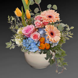 Mixed bouquet of pink, peach, blue, and orange flowers in a white vase