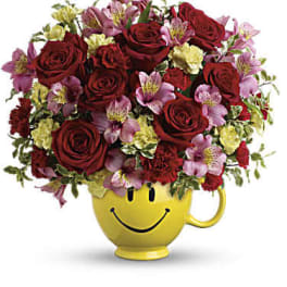 Bouquet of red roses and pink flowers in a yellow smiley-face mug