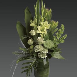 Green floral arrangement in a glass vase with tropical leaves and pale blooms
