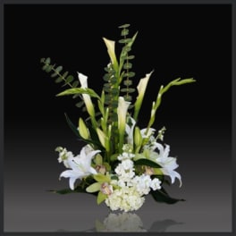 Tall white lily arrangement with green foliage on a dark background