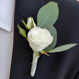 White rose boutonniere with green leaves on a dark suit