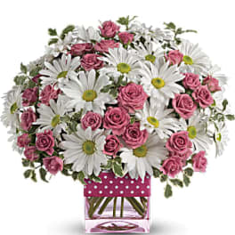 Pink roses and white daisies in a square glass vase with a polka-dot ribbon