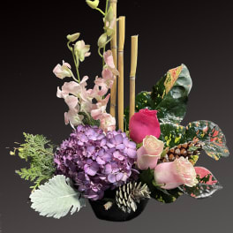 Pink roses and purple hydrangea in a black vase with bamboo and pinecones