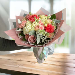 Hand-tied bouquet of pink and cream roses wrapped in pastel paper