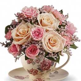 Pink and cream roses arranged in a floral teacup with saucer