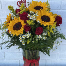 Bouquet of sunflowers, red roses, and daisies in a glass vase with a red ribbon