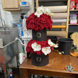 Two-tier arrangement of red roses with white orchids in black hat boxes