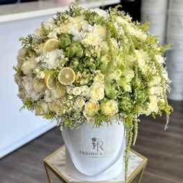 Large cream and green floral arrangement in a white hatbox with lemon slices