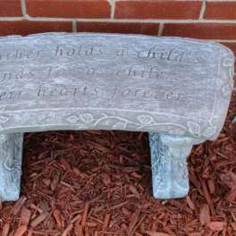 Decorative stone bench with an engraved quote in a garden bed