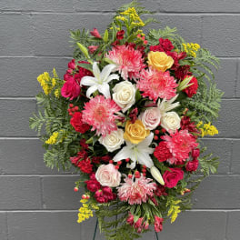 Standing floral spray with pink, white, and yellow blooms on an easel