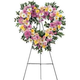 Heart-shaped floral wreath on a metal easel with pink, white, and yellow flowers