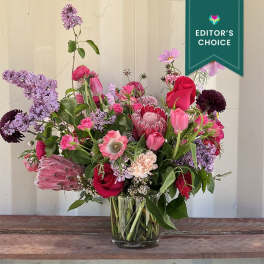 Mixed bouquet of pink, red, and lavender flowers in a glass vase