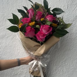 Bouquet of pink roses with small yellow flowers wrapped in brown paper