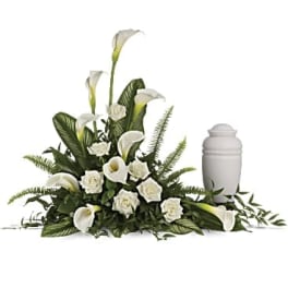 White calla lilies and roses arranged beside a white urn