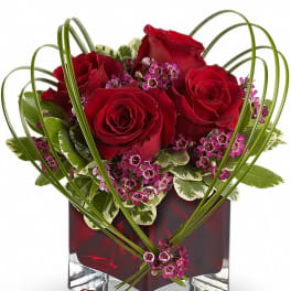 Red roses and purple filler flowers in a square glass vase