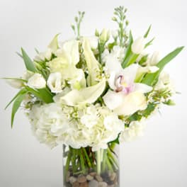 White floral arrangement in a glass vase with stones