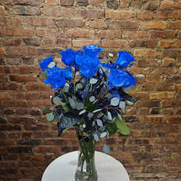 Blue roses arranged in a clear glass vase with mixed foliage