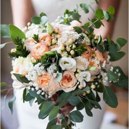 Bride holding a bouquet of peach and white flowers with greenery