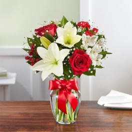 Bouquet of red roses and white lilies in a glass vase with a red ribbon