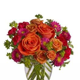 Orange roses and magenta daisies in a clear glass vase