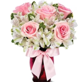 Pink roses and white alstroemeria in a red vase with a pink ribbon