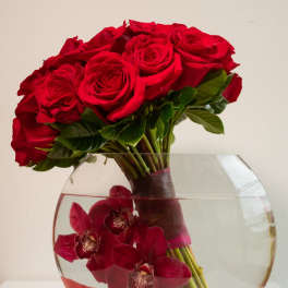 Red roses and dark red orchids arranged in a round glass vase