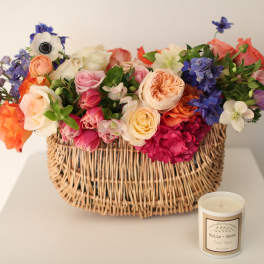 Mixed bouquet in a wicker basket with a candle beside it