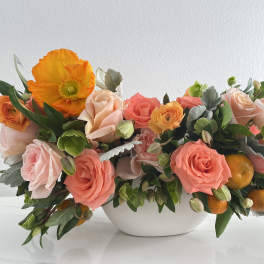 Coral and peach roses with orange poppies in a white bowl vase