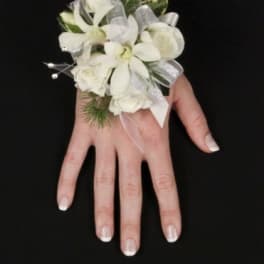 White floral wrist corsage with silver ribbon on a hand