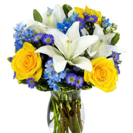 Bouquet of white lilies, yellow roses, and blue flowers in a glass vase