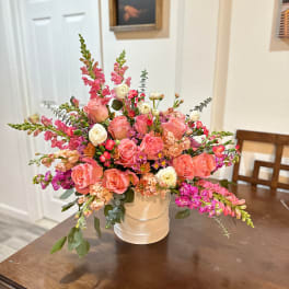 Pink and peach floral arrangement in a white hatbox-style container